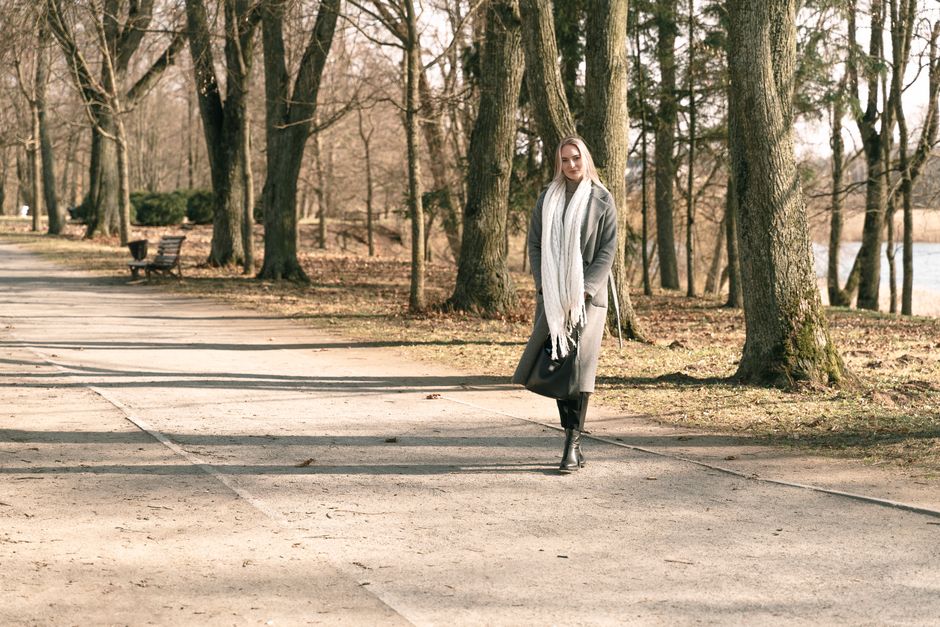 A woman strolls down a tree-lined path in a serene park, wearing a coat and scarf.