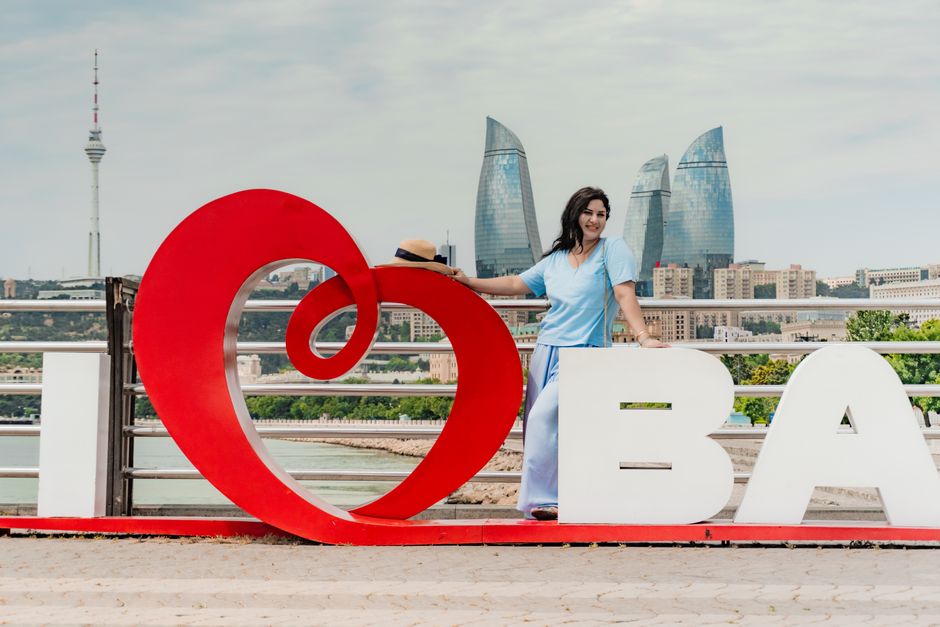 Woman standing by 'I Love Baku' sign with Flame Towers in background.