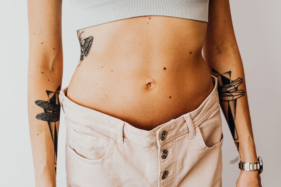 Close-up of a tattooed woman's torso wearing high-waisted pants, showcasing body art and style.