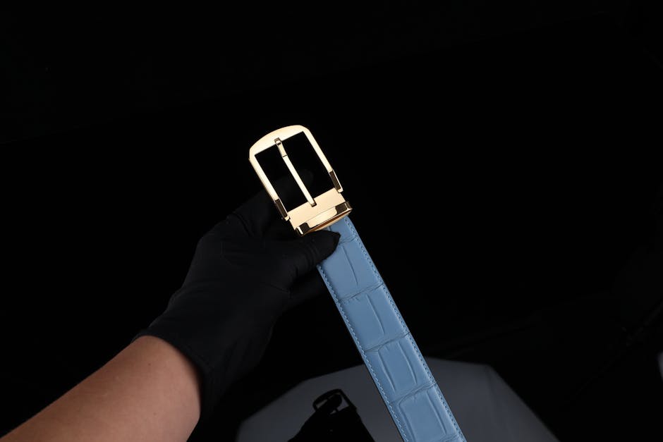 Luxurious blue leather belt featuring a chic gold buckle held by a gloved hand.