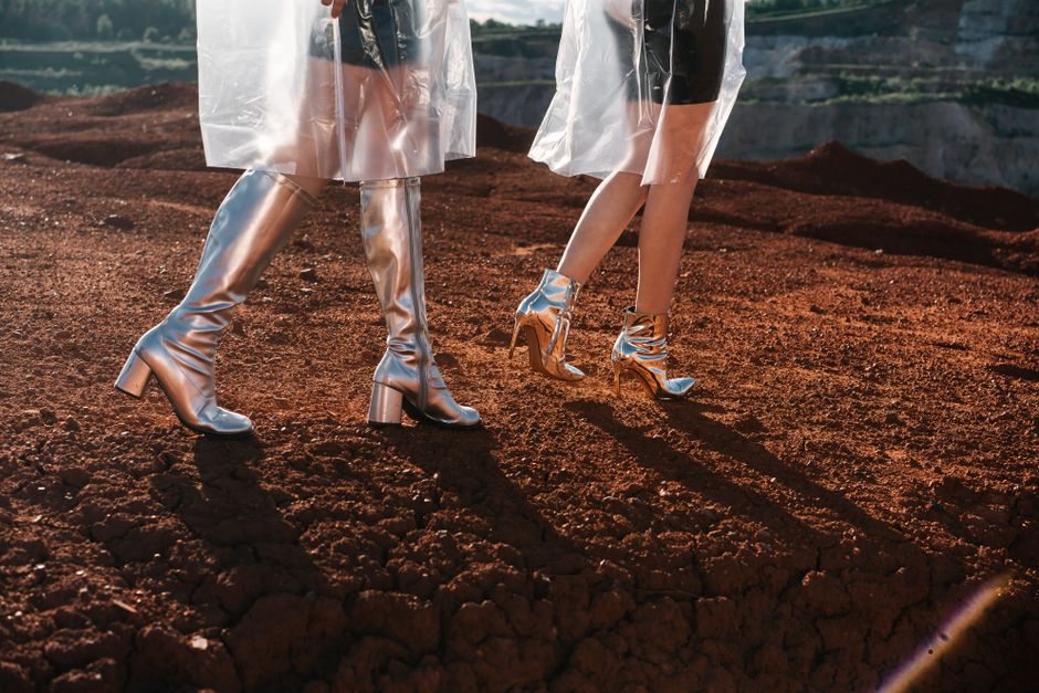 Stylish silver boots with transparent raincoats on a red earth landscape.