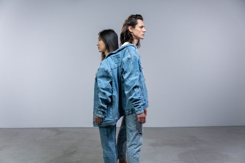 Two models in denim jackets and jeans standing back-to-back. Modern fashion style.