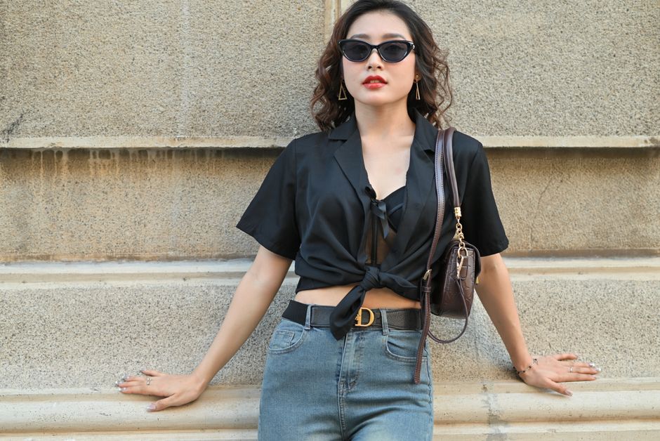 Chic woman in black shirt and jeans leaning against an urban wall.