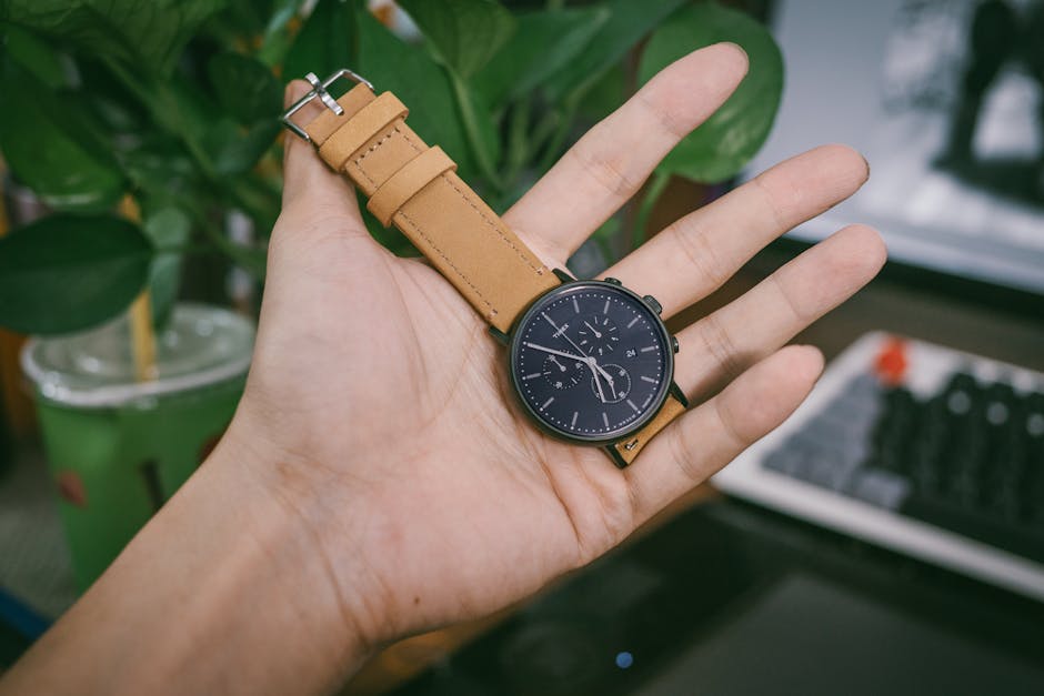 A close-up image of a hand holding a stylish wristwatch with a leather strap indoors.