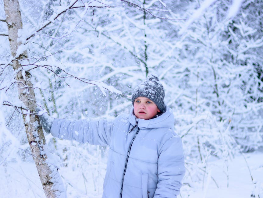 A child stands in a snowy winter forest, dressed warmly in a coat and hat.