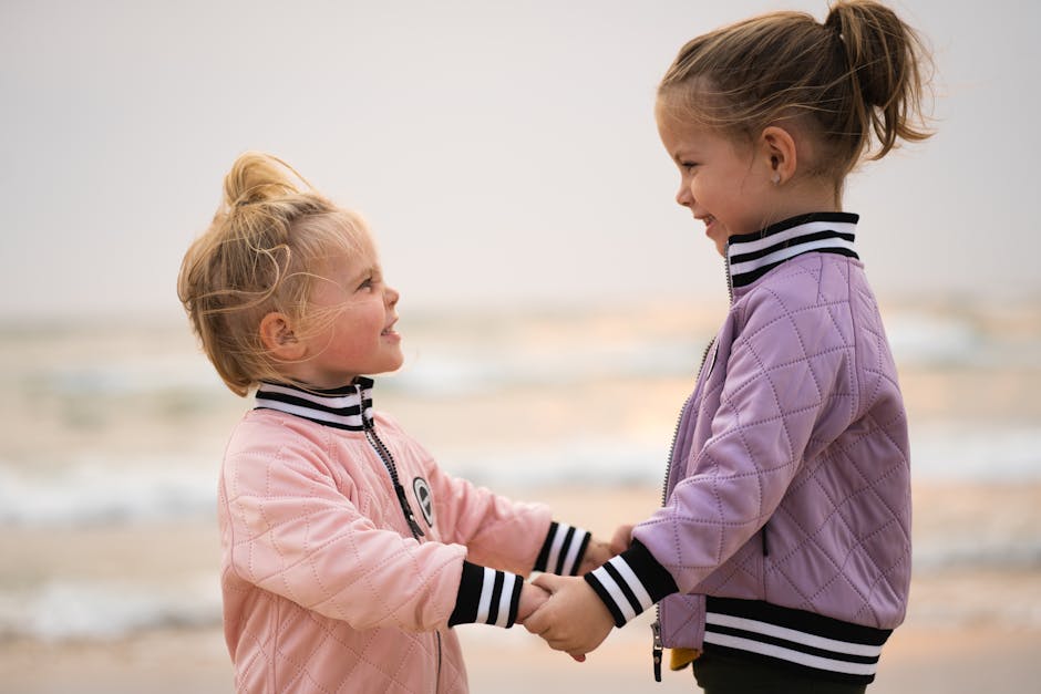 Two young girls smiling and holding hands on a beach, showcasing love and togetherness.