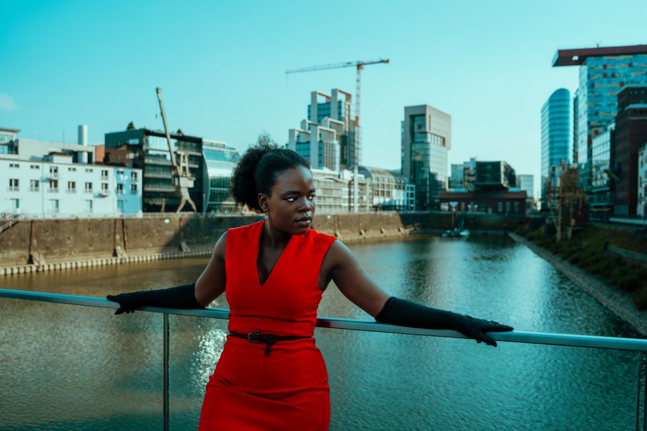 Stylish woman in a red dress with black gloves poses on a modern city bridge.