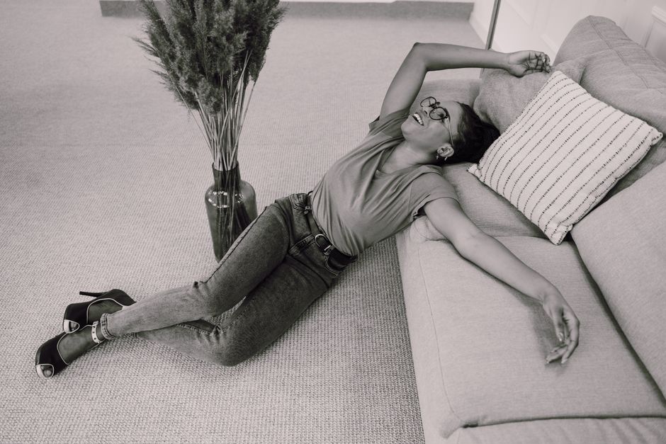 Black and white photo of a smiling woman posing on the floor beside a couch.
