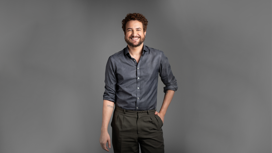 Portrait of a smiling man in casual attire on a gray background.