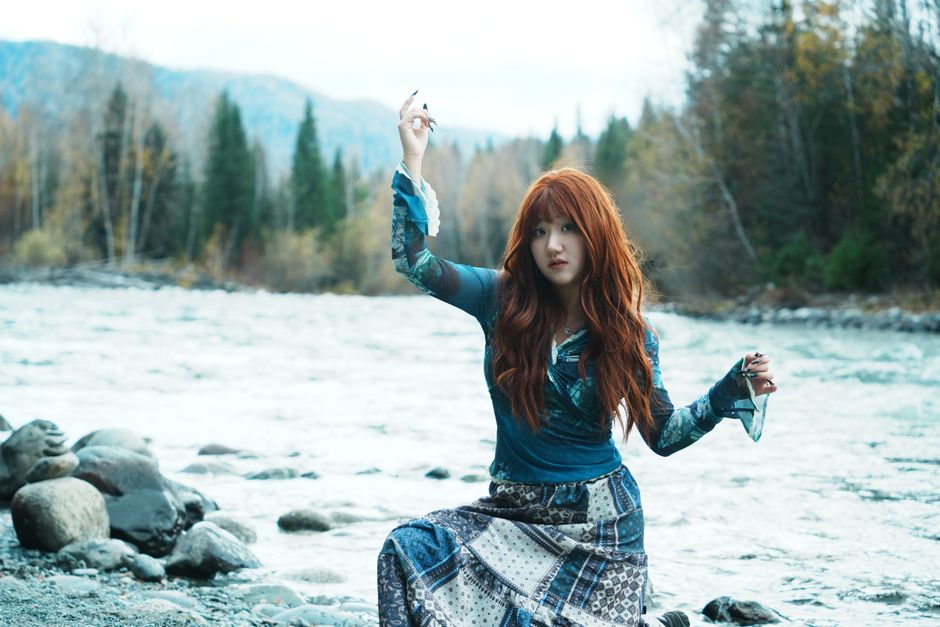 A woman with red hair by a river, creating a serene and natural atmosphere.
