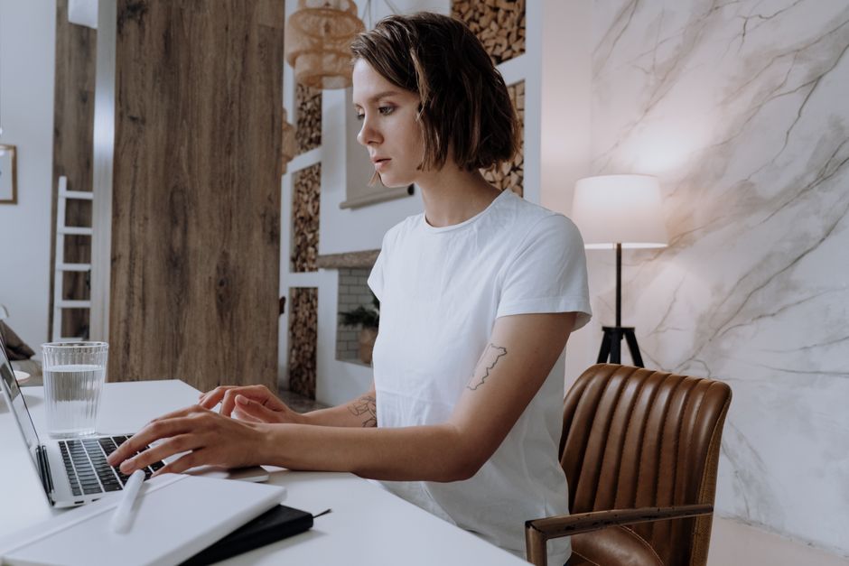 Young woman with short hair works remotely on laptop at stylish home office, featuring modern decor and natural light.