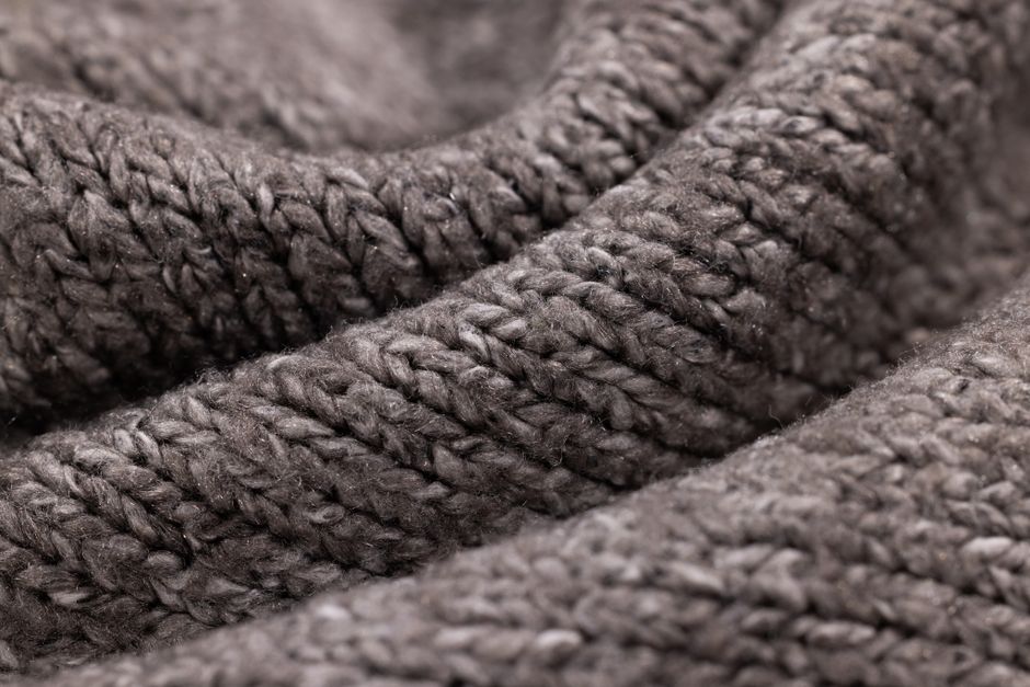 Close-up image of a textured gray woolen fabric, showing intricate knitting patterns.