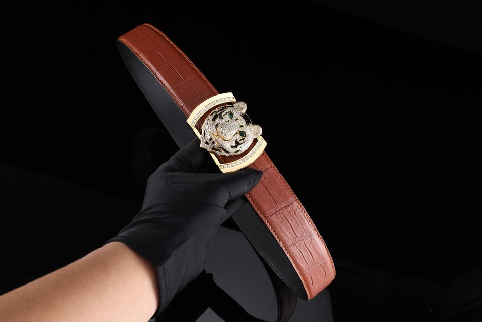 Elegant brown leather belt featuring an intricate decorative buckle, held by a gloved hand.