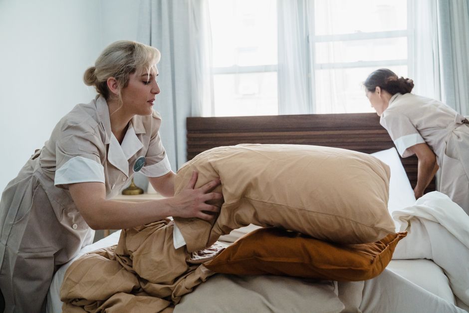 Hotel housekeeping staff efficiently clean and arrange a guest room bed.