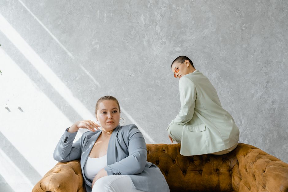 Two stylish women in suits, sitting on a couch, exemplifying body positivity.