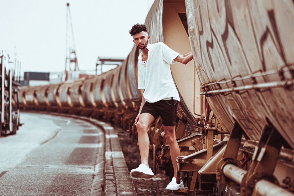 Stylish man in casual attire posing alongside industrial train cars.