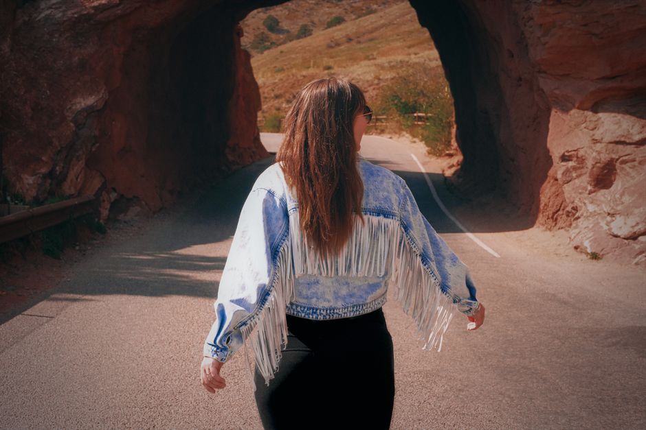 Woman in fringed jacket walking through a picturesque tunnel in Morrison, Colorado, on a sunny fall day.