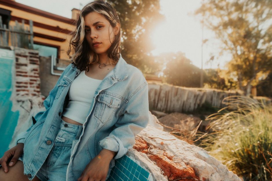 Young woman in denim jacket posing outdoors during golden hour.