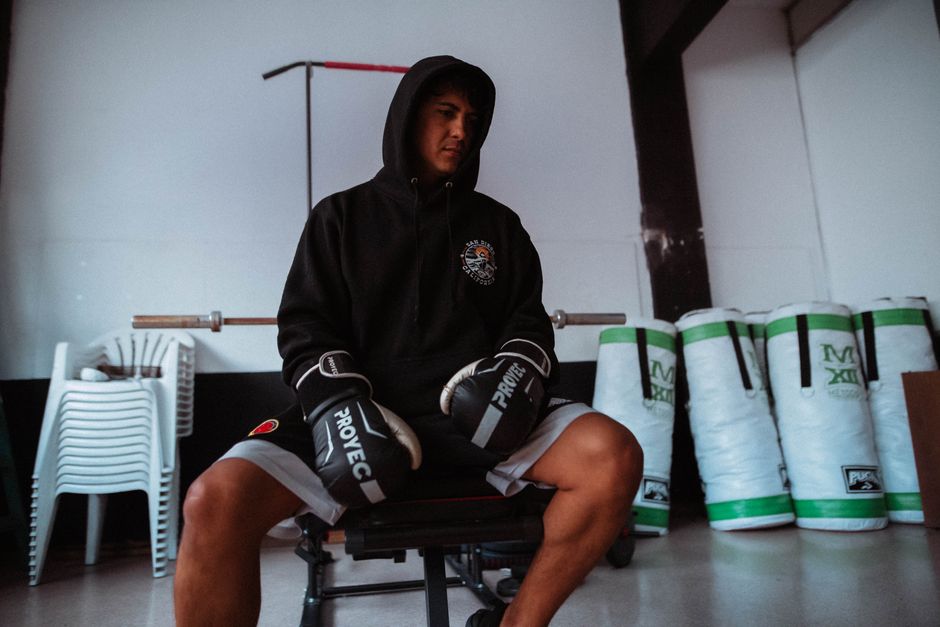 A boxer in a hoodie and gloves takes a break in a gym, Buenos Aires.