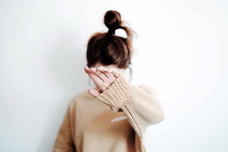 A woman in a sweatshirt raises her hand to cover her face, suggesting stop or privacy.