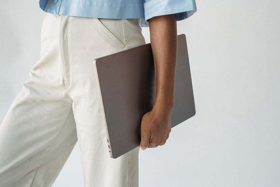 Close-up of a person holding a laptop in a minimalist fashion setting.