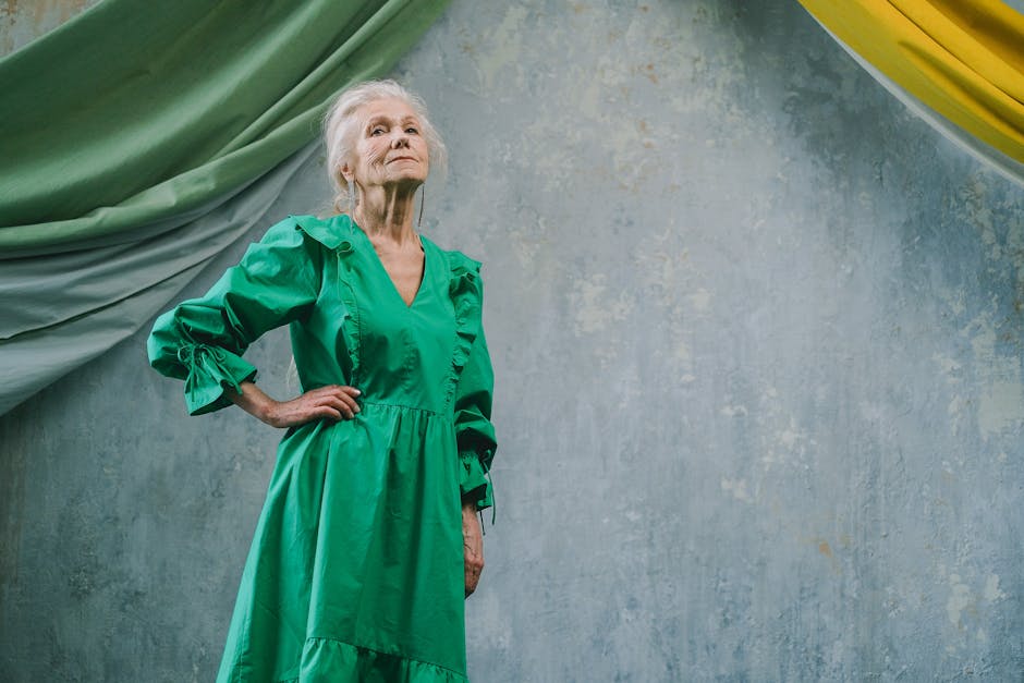 Portrait of an elderly woman confidently posing in a green dress against a textured blue background.