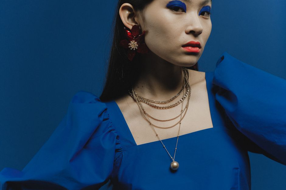 Stylish portrait of a woman in blue attire with vibrant makeup and gold jewelry.