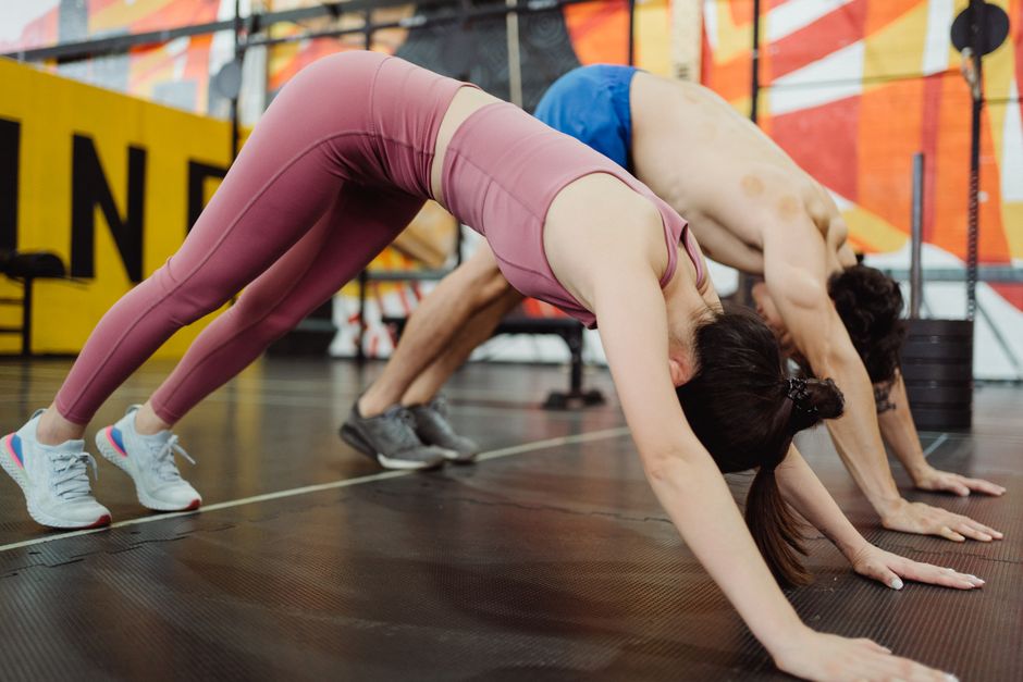 Two individuals engaged in stretching exercises in a colorful gym setting, showcasing fitness and flexibility.