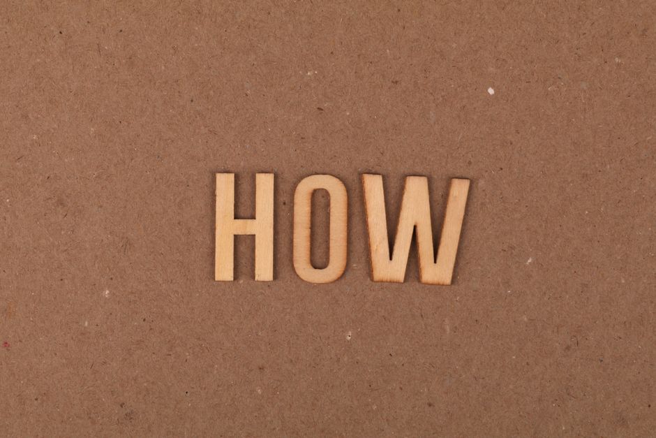Wooden letters spelling 'HOW' on brown textured cardboard background.