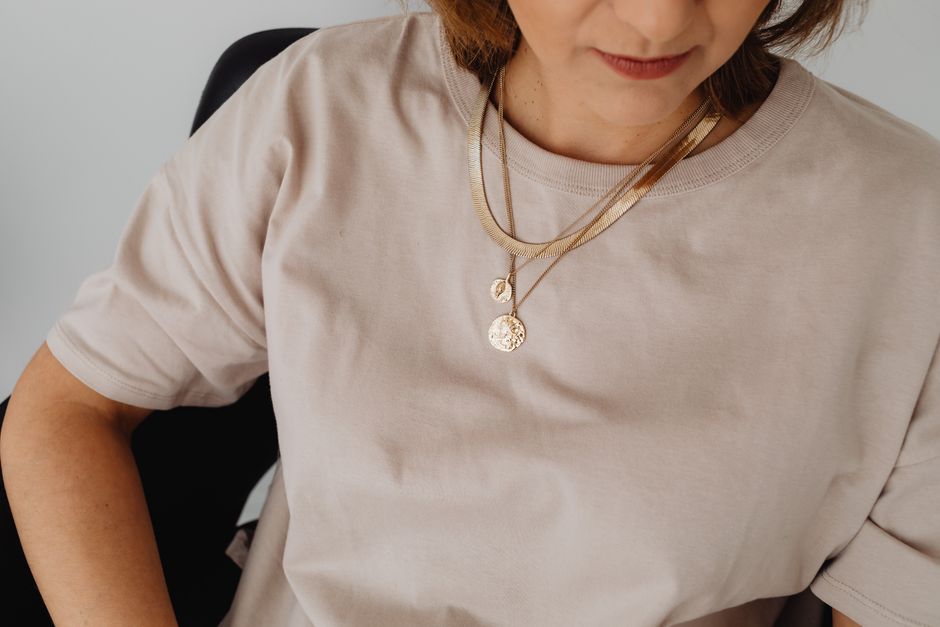 Close-up of a woman wearing a beige shirt with a layered gold necklace.