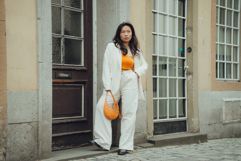 Stylish woman in a white suit and orange crop top posing in an urban setting. Perfect for fashion shoots.