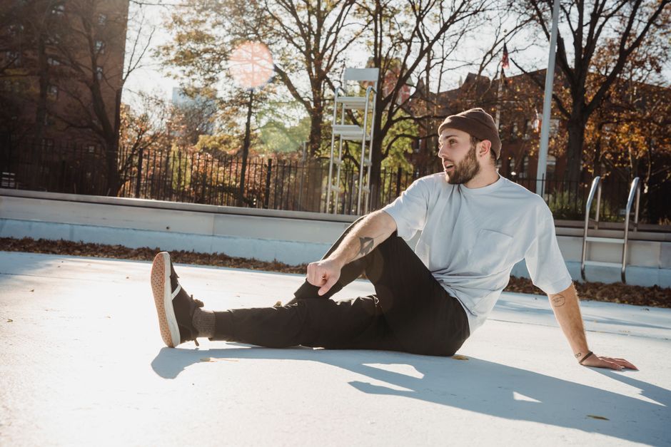 Thoughtful male in trendy clothes sitting in empty pool without water on street in residential district in sunny day