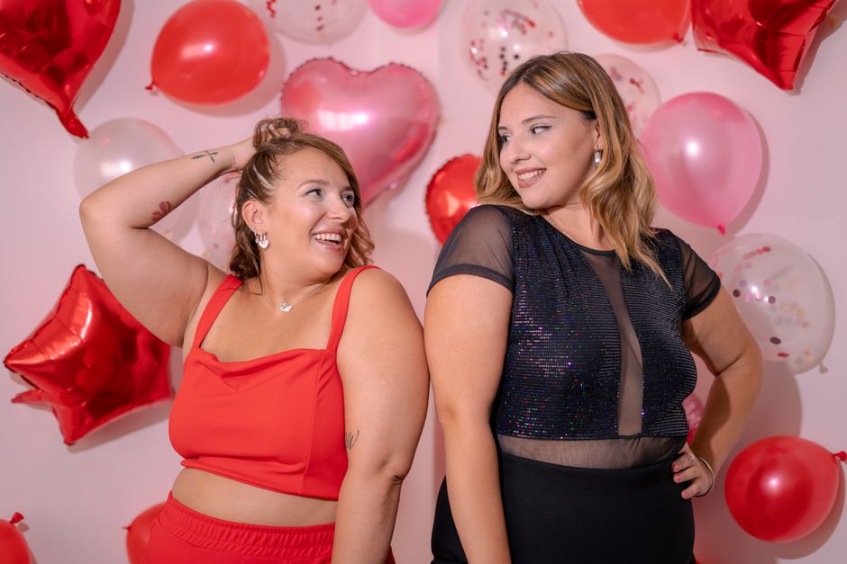 Two women enjoying a celebration with heart-shaped and pink balloons, exuding happiness and style.
