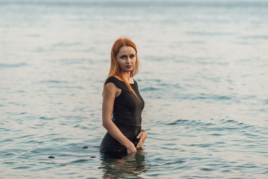A woman in a black dress gracefully standing in the calm sea during the day.