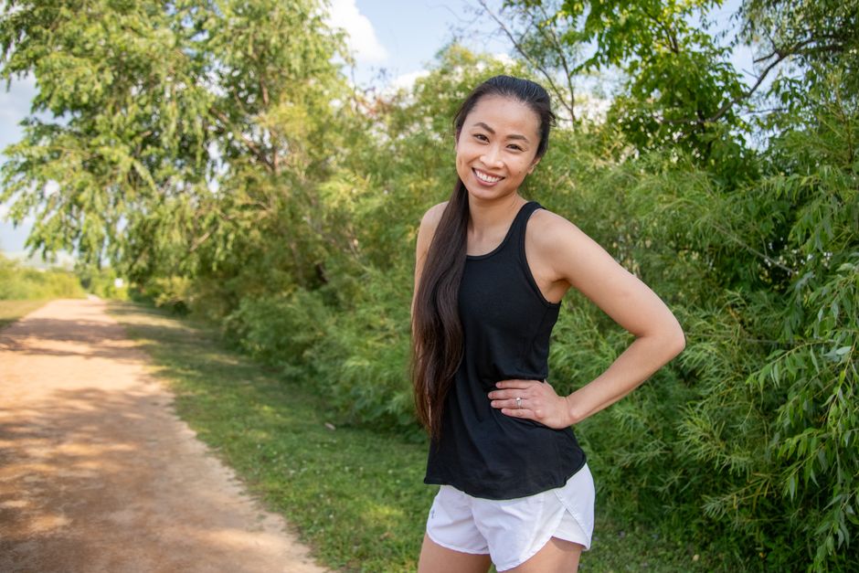 Asian woman in black tank top and shorts smiling outdoors on a sunny day.