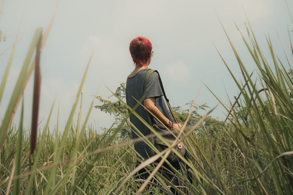 A woman with red hair explores a grassy field under a bright sky, embracing nature.