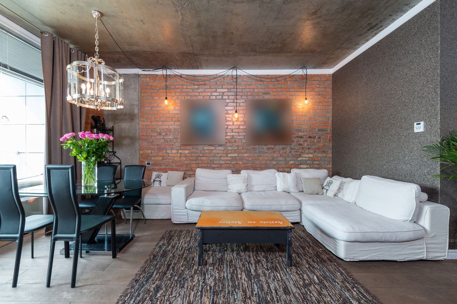 Stylish living room featuring industrial design with brick wall, white sofa, and chic chandelier.