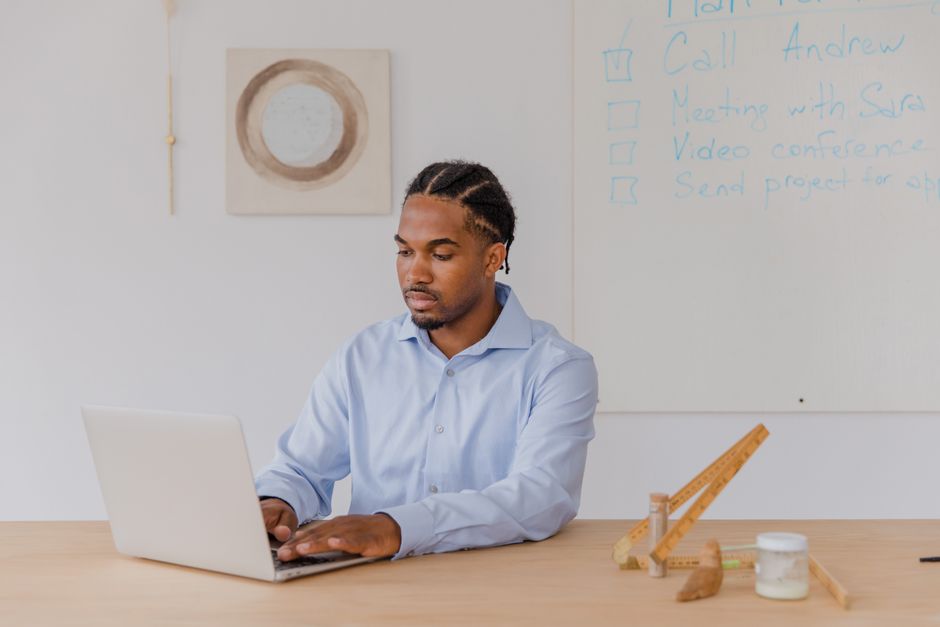 Businessman using laptop at desk with whiteboard notes in modern office environment.