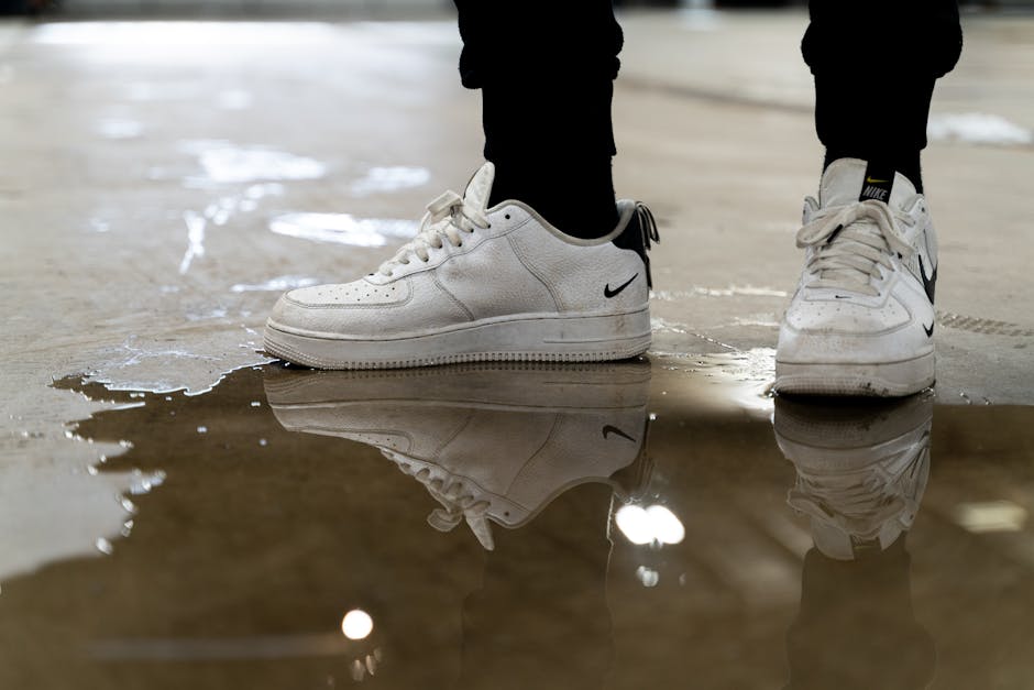 A pair of white sneakers reflected in a puddle on an indoor surface, creating an artistic perspective.