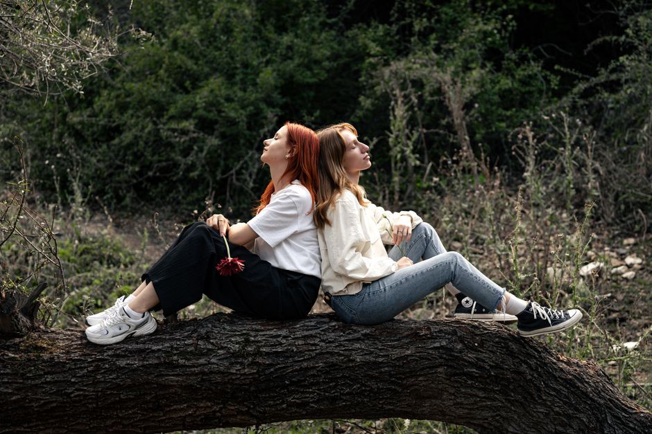 Two women sitting peacefully on a tree branch in a serene forest setting.