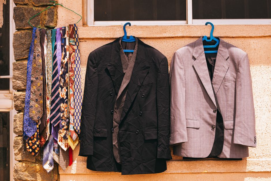 A black and gray suit with colorful ties hanging outdoors on a wall in Jos, Nigeria.