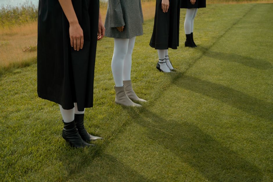 Three women in boots and dresses casting shadows on grass.