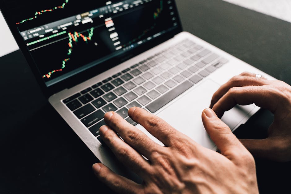 Close-up of hands typing on a laptop with stock market graphs, ideal for finance or business themes.