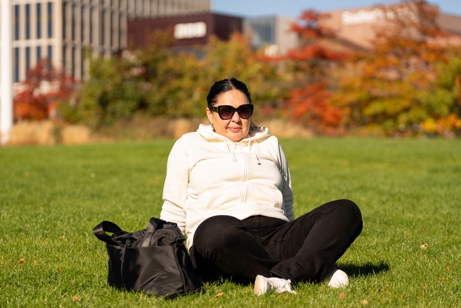 Woman in sunglasses enjoying a sunny autumn day outdoors, seated on grass.
