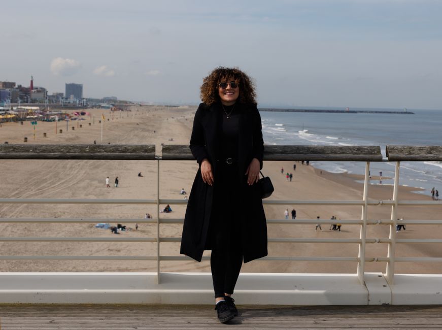 Woman in black standing on boardwalk overlooking the beach on a clear day.