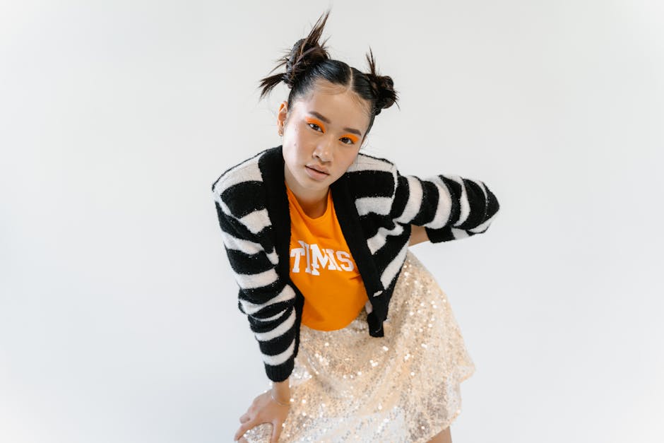 Dynamic portrait of a young woman in stylish street wear with bold eye makeup against a white background.