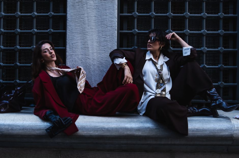 Two fashionable women in stylish outfits posing against an urban backdrop.